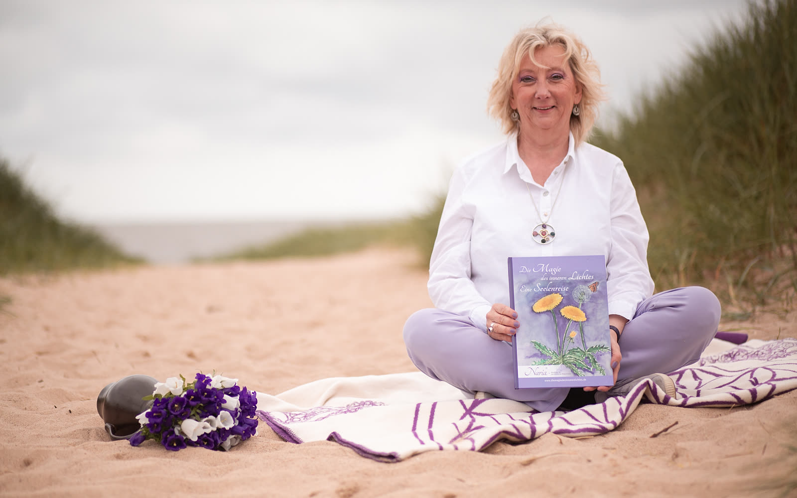 Naria sitzt mit ihrem Buch in den Dünen